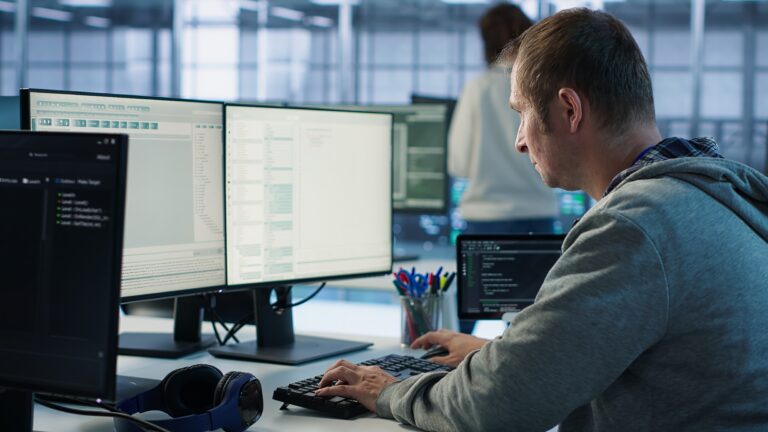 Programer fokusiran na rad za dva monitora u modernom open-space IT kancelarijskom prostoru